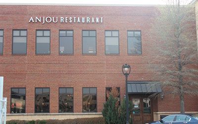 The brick facade of Anjou Restaurant featuring two levels of windows and a street lamp by the entrance.