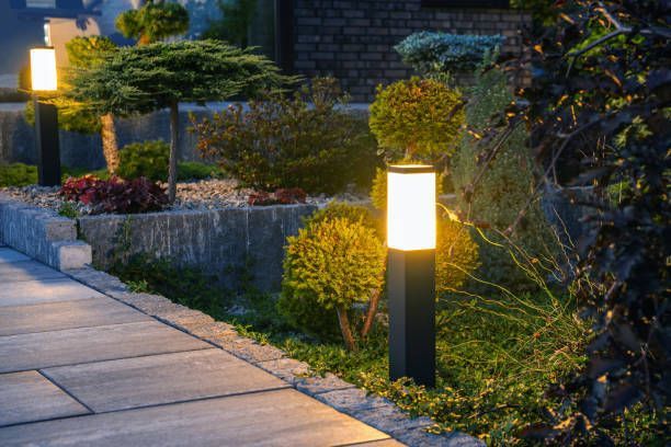 A stone garden path illuminated at night by glowing square post lights, surrounded by shrubs and ornamental trees.