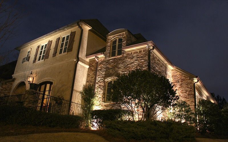 A large stone and stucco house at night, illuminated by warm outdoor accent lighting.
