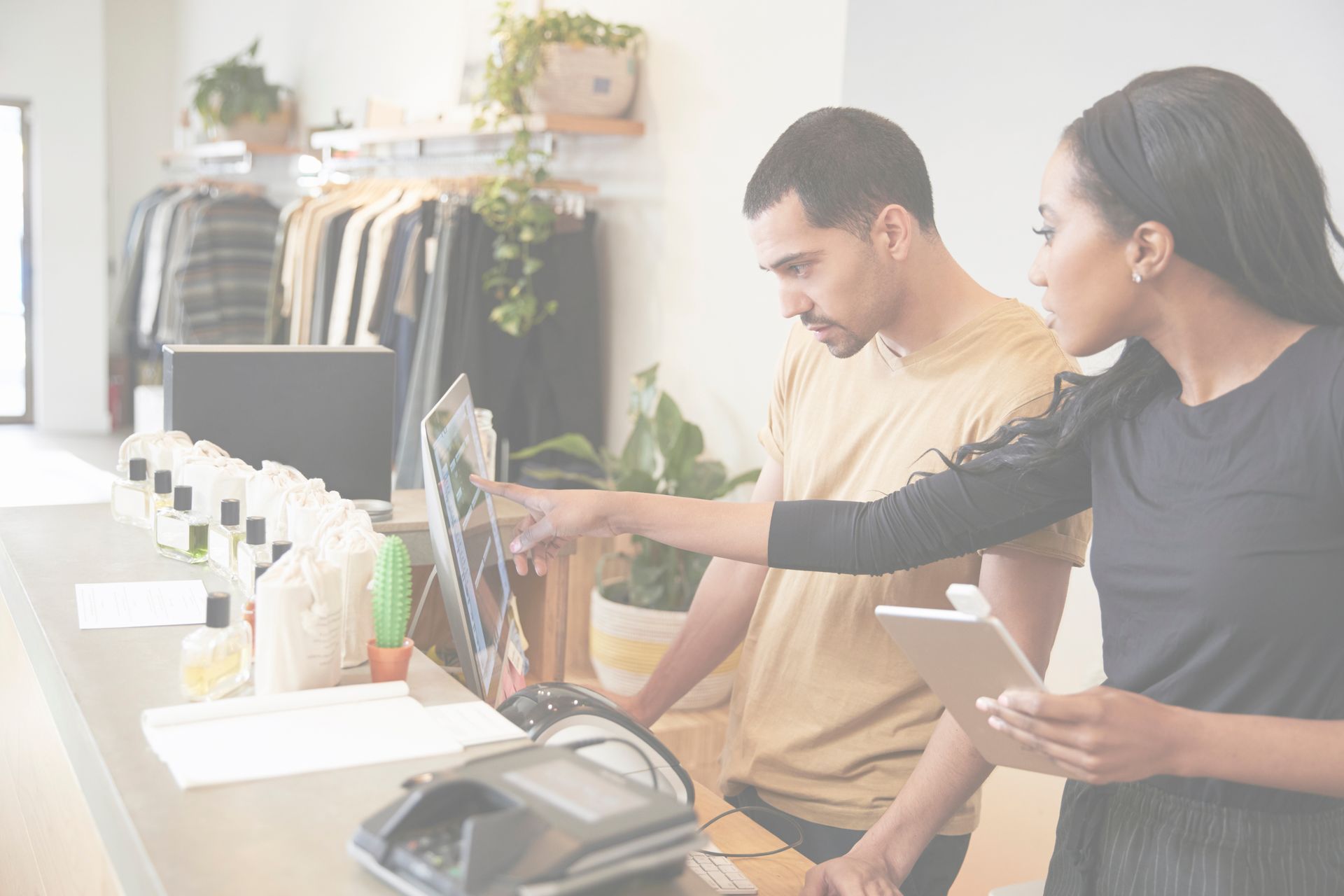 Image 12: A man and woman retail employees looking at POS systems in fashion store. Image is for retail staffing