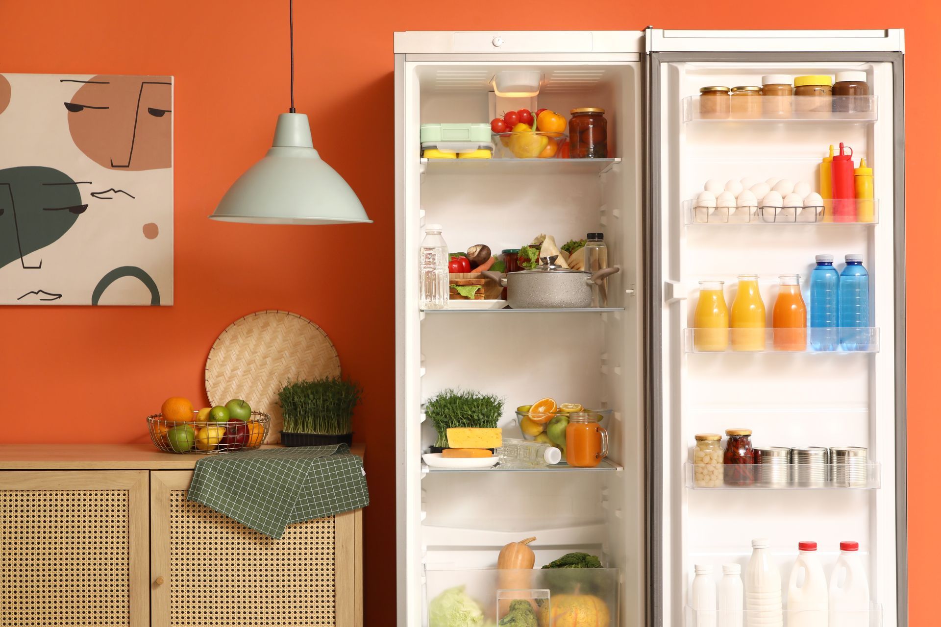 Open refrigerator filled with food, in a brightly colored room with a hanging lamp.