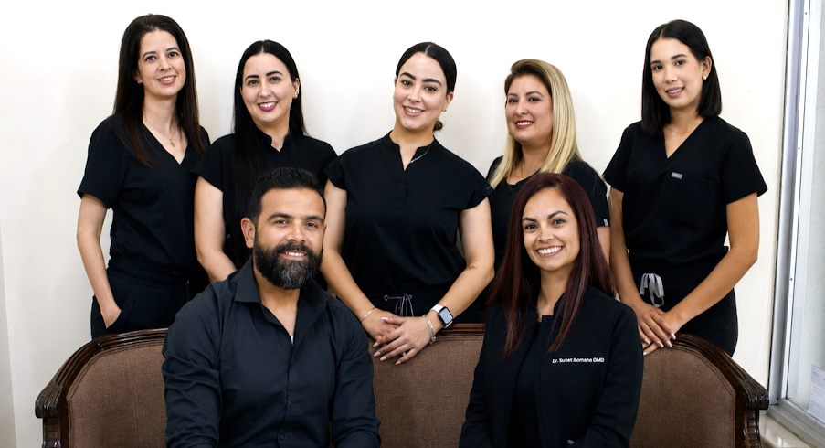 A group of six dental professionals in black scrubs pose in an office setting.