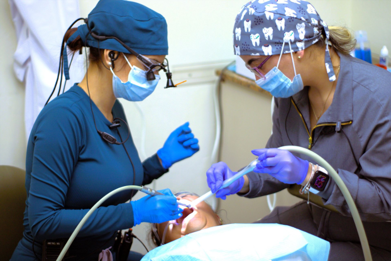 Two dentists in masks and gloves treating a patient in a dental clinic