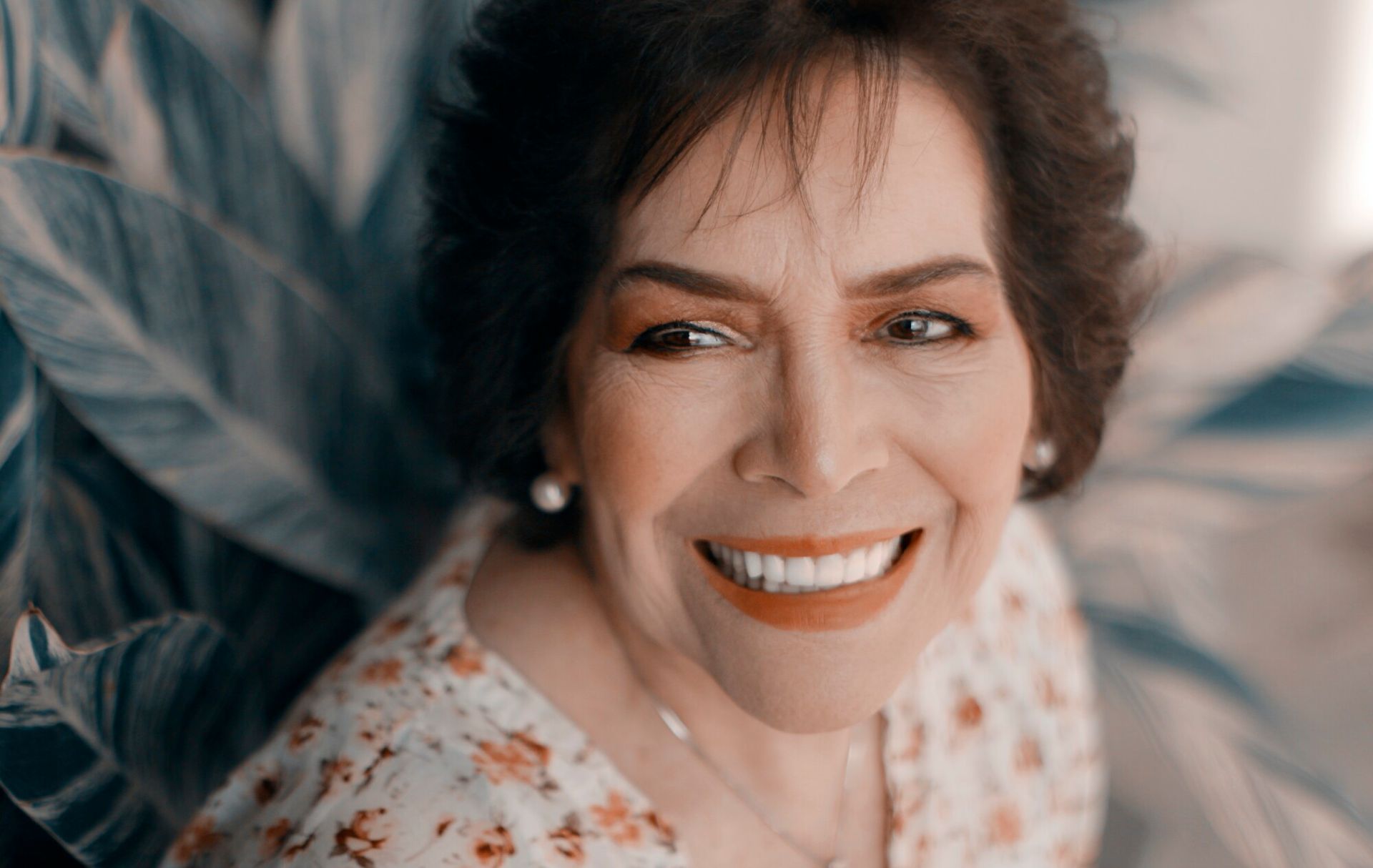 An elderly woman is smiling for the camera while laying on a bed.