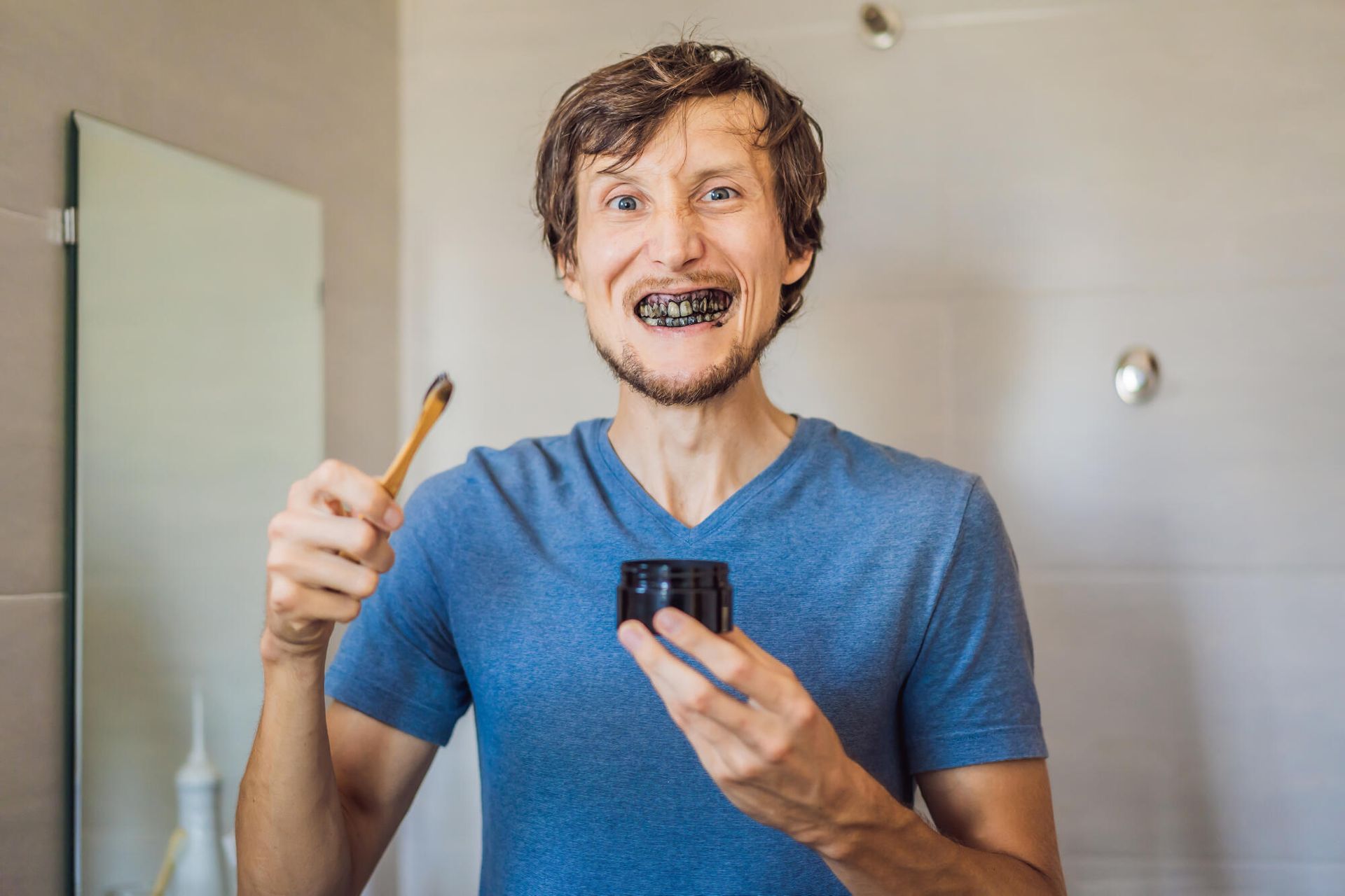 A man is brushing his teeth with black toothpaste in a bathroom.