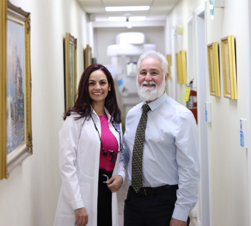 Woman in lab coat and man in tie smiling next to a door with a phone number.