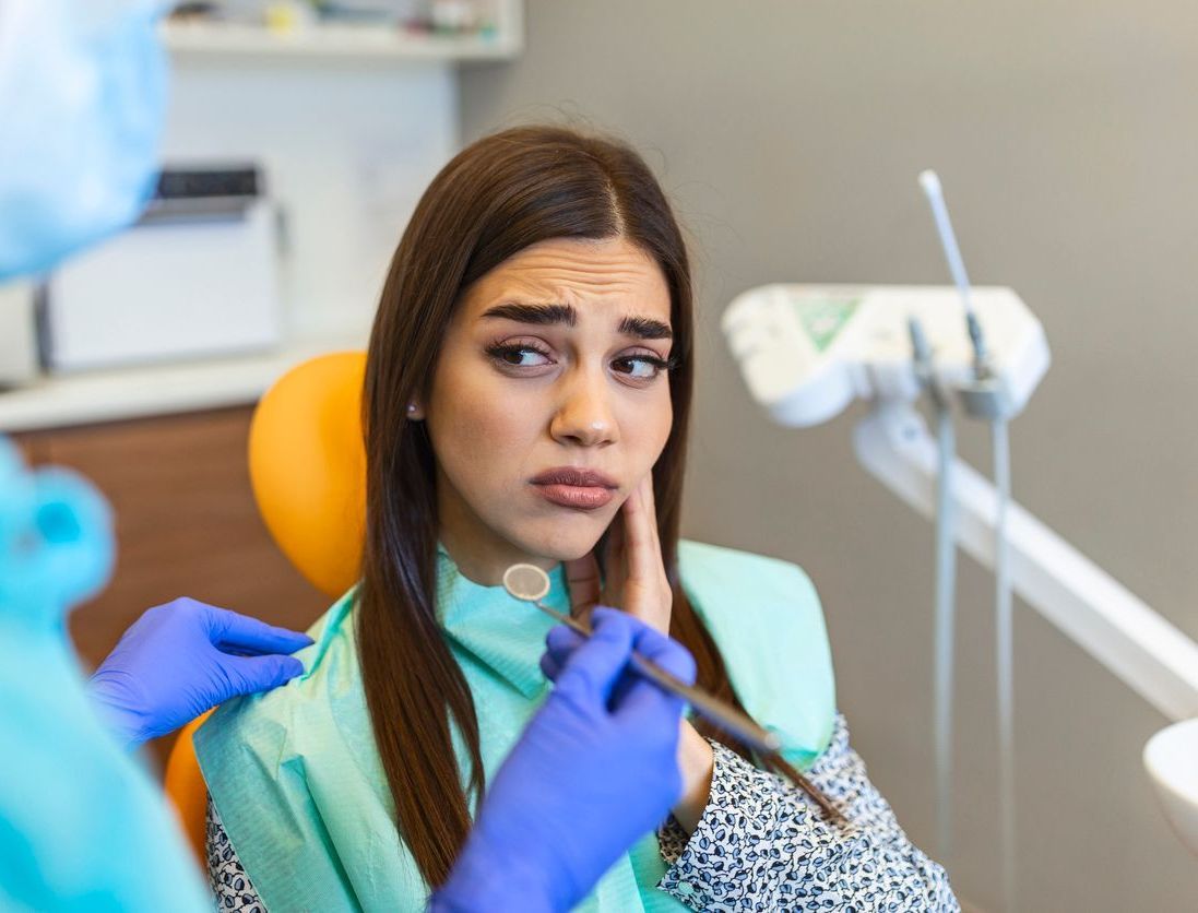 A woman is sitting in a dental chair with a dentist examining her teeth.