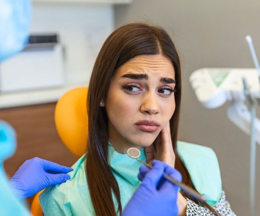 Una mujer está sentada en una silla dental con dolor de muelas.