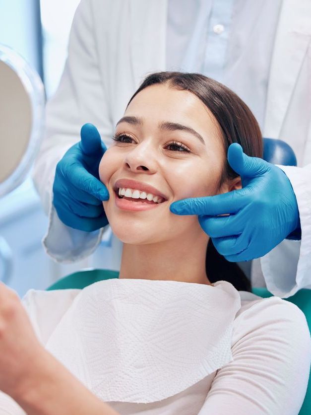 A woman is sitting in a dental chair while a dentist examines her teeth.