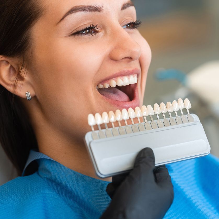 Una mujer está sentada en una silla dental con la boca abierta y una tabla de colores de dientes frente a ella.