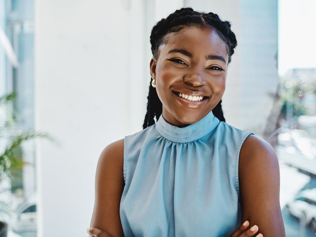 A woman in a blue shirt is smiling with her arms crossed.