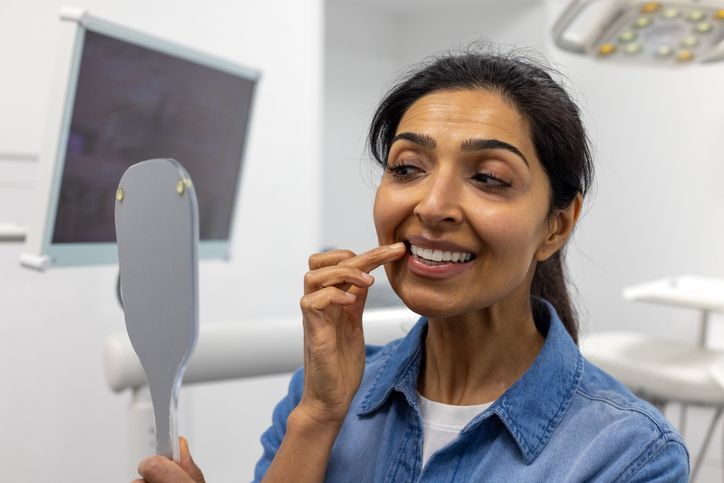 Woman checking her teeth in a mirror, smiling in a bright bathroom.