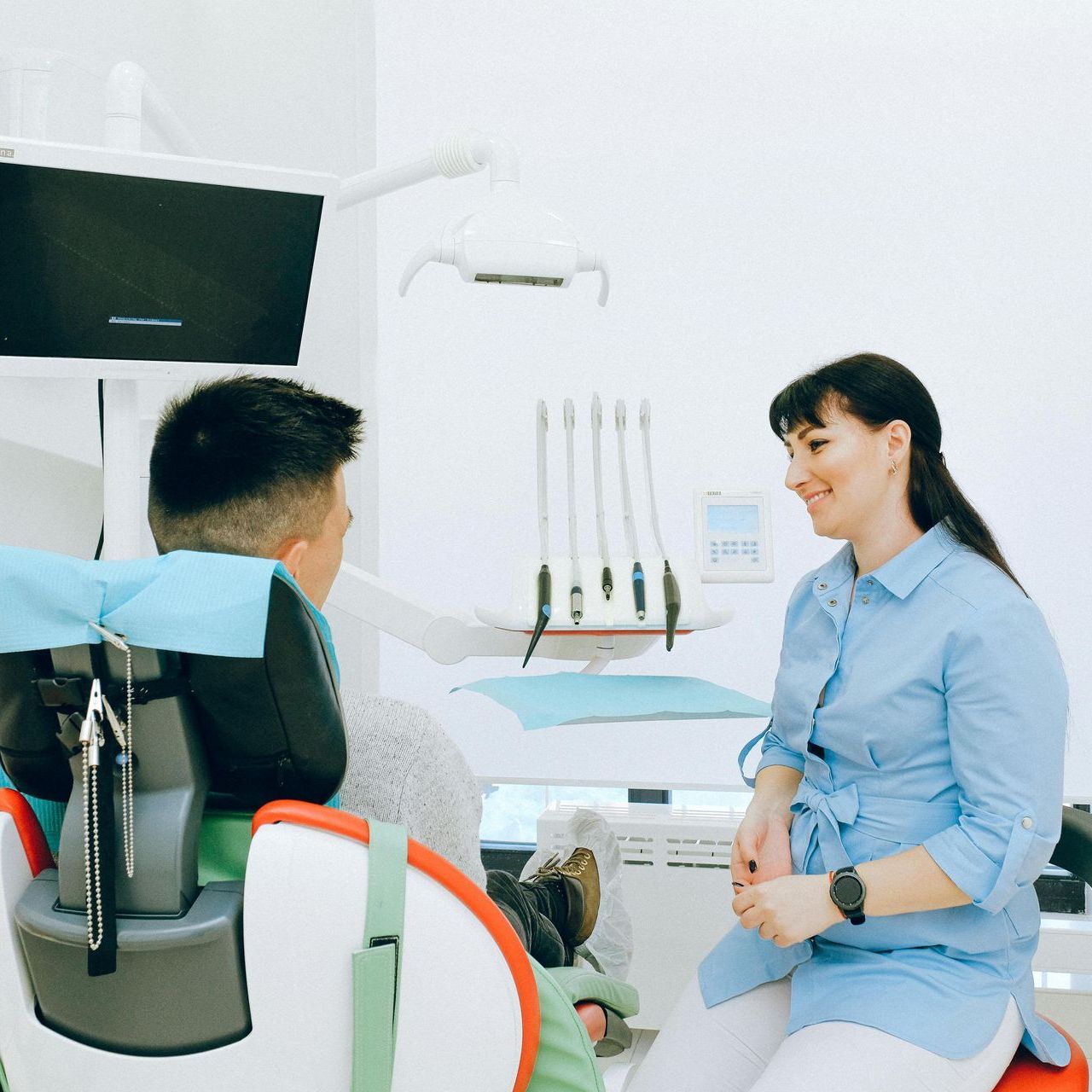 Una mujer está hablando con un hombre en una silla dental.