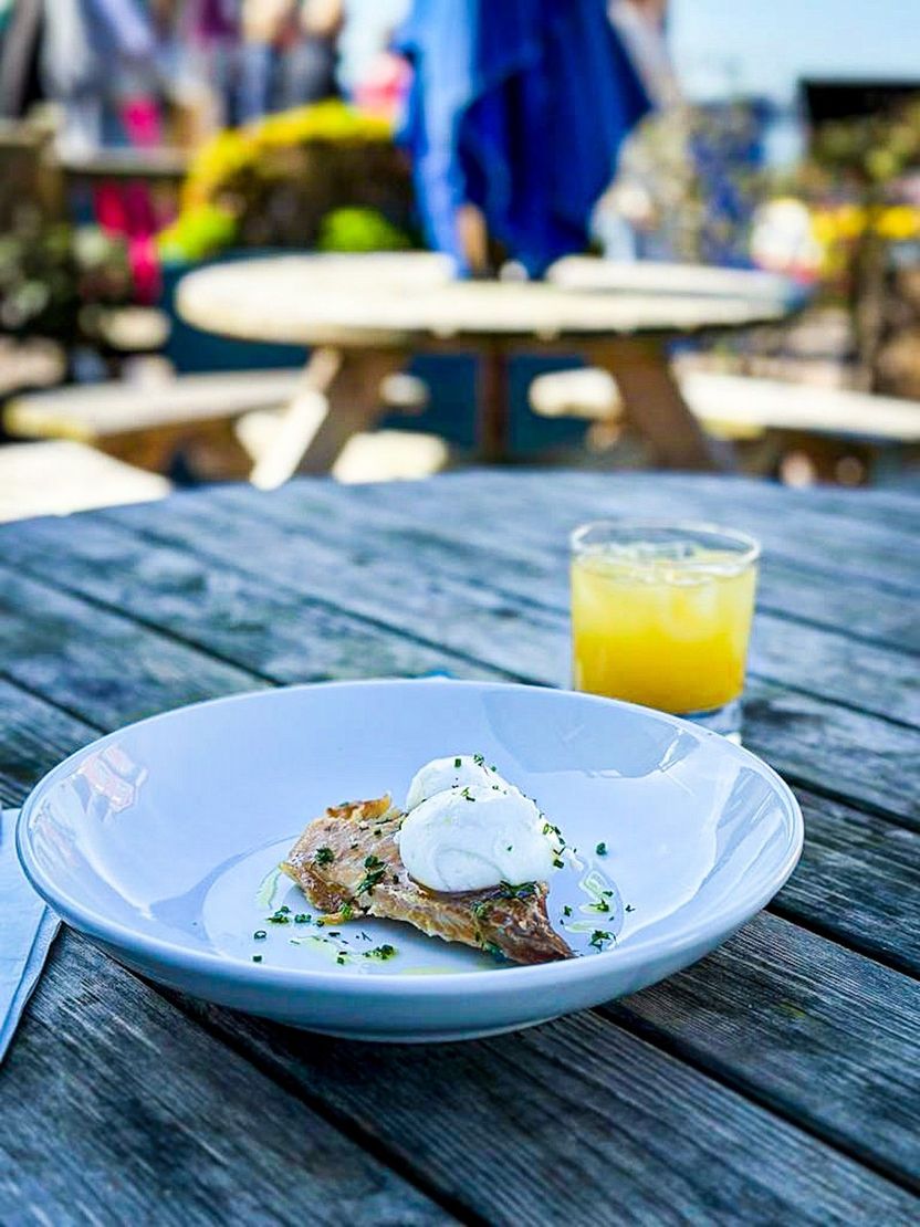 Haddock, poached eggs, and chives, on a white plate, on a table outside with a glass of orange juice.