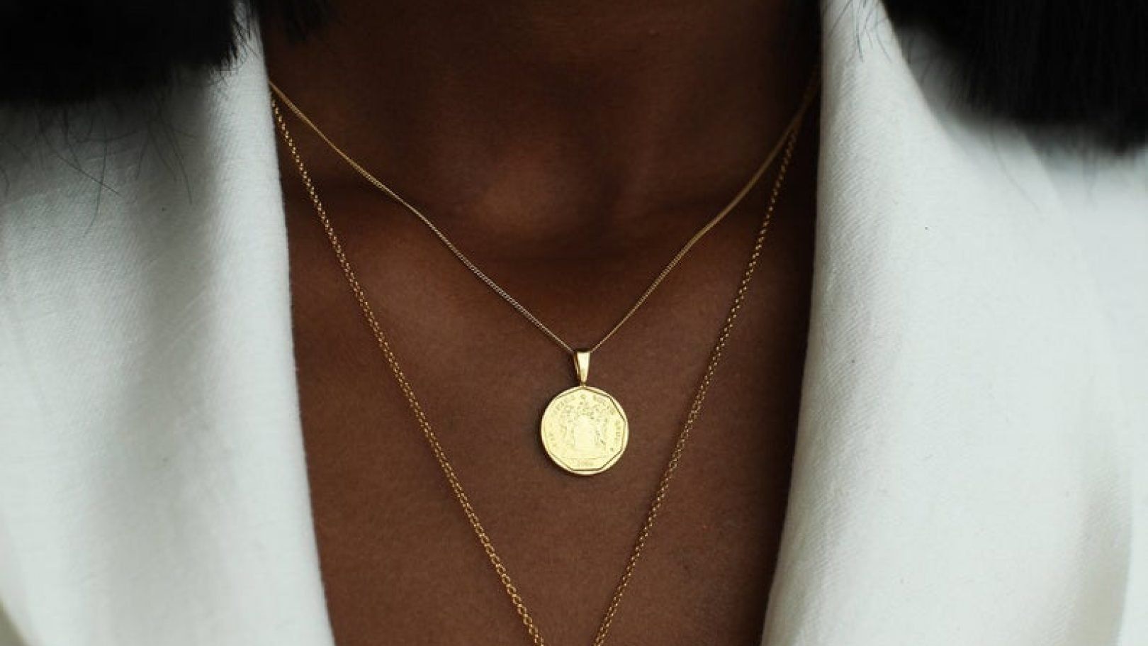 a woman wearing a gold necklace with a coin pendant