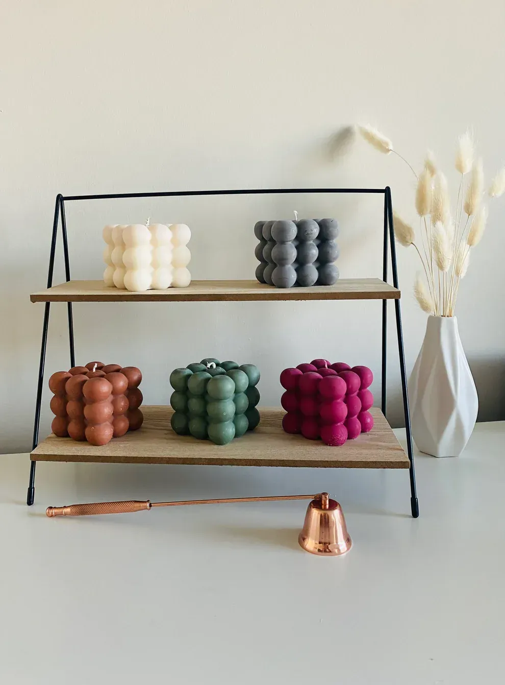 three different colored candles are on a wooden shelf