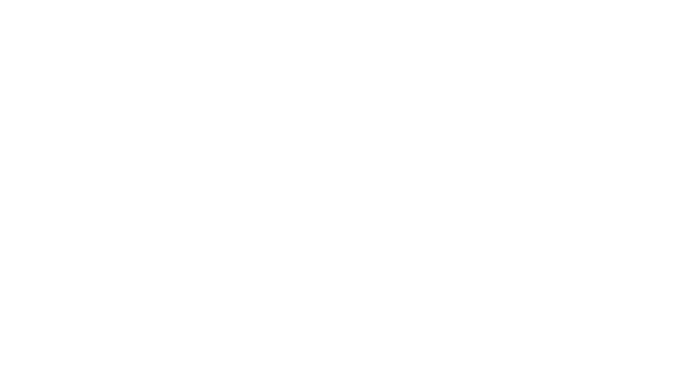 A person sits on a colorful, patterned rug in a sunlit room, playing a light-colored acoustic guitar.