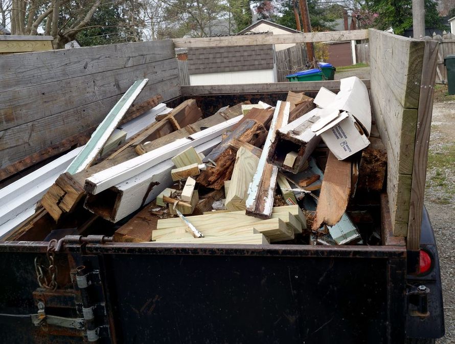 A utility trailer filled with construction debris, including wood planks, trim, and miscellaneous building materials.