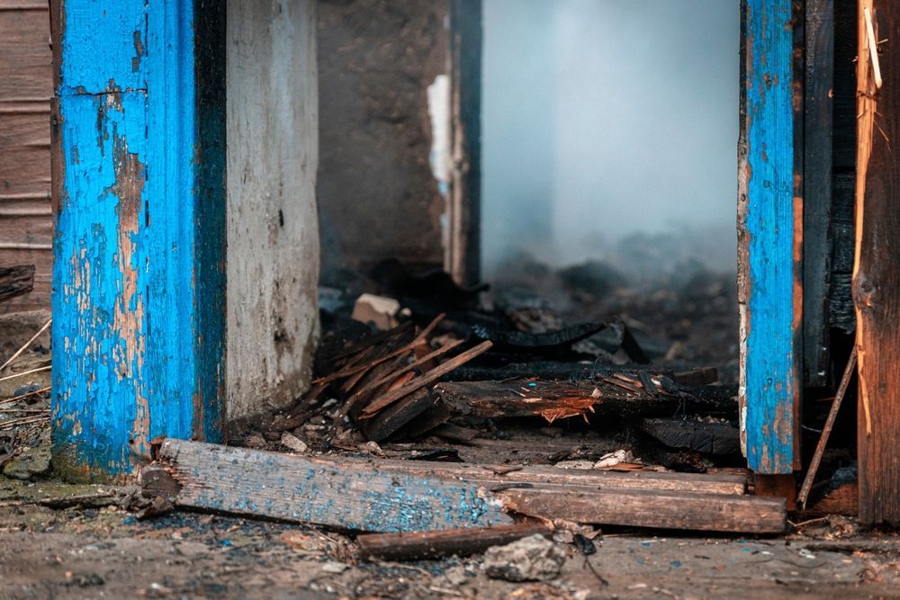 A doorway frames the interior of a fire-damaged building, showing charred debris and lingering smoke.