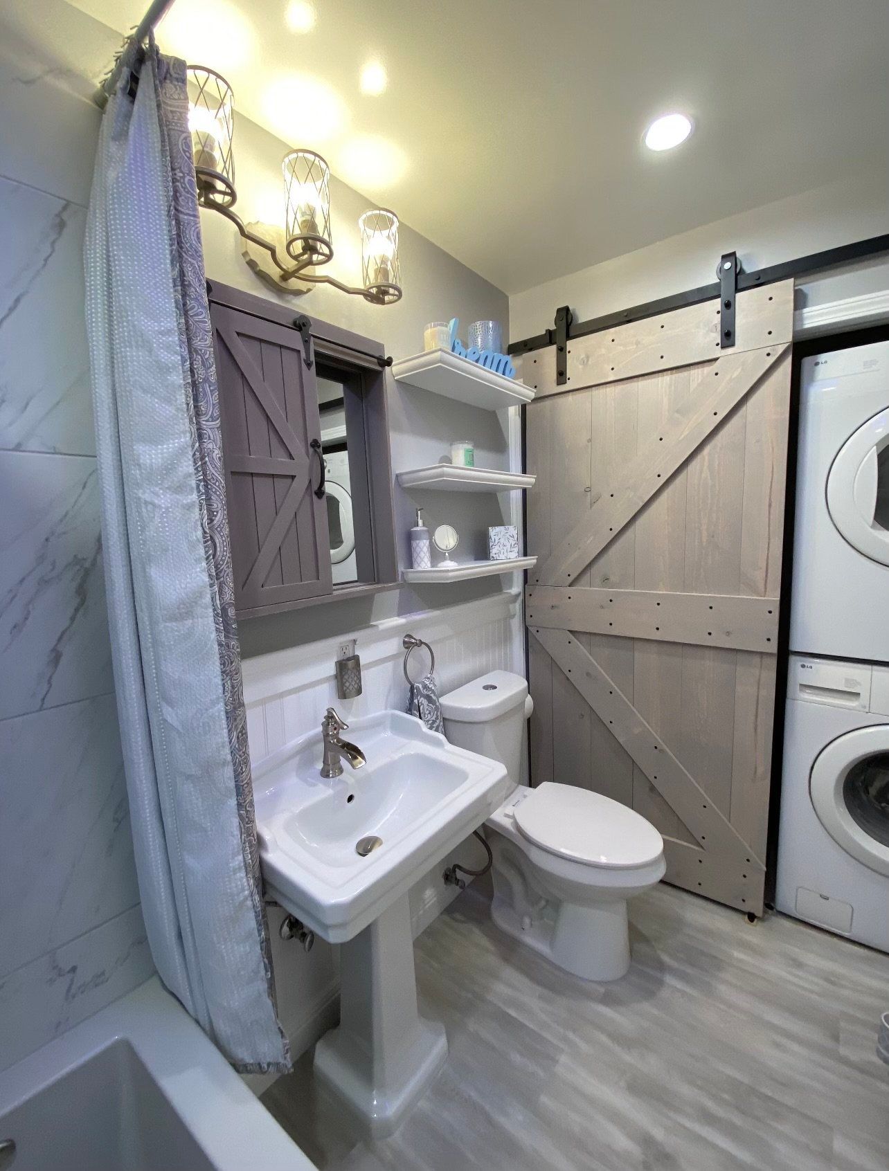 Bathroom with pedestal sink, toilet, shelving, and sliding barn door hiding stacked washer/dryer.