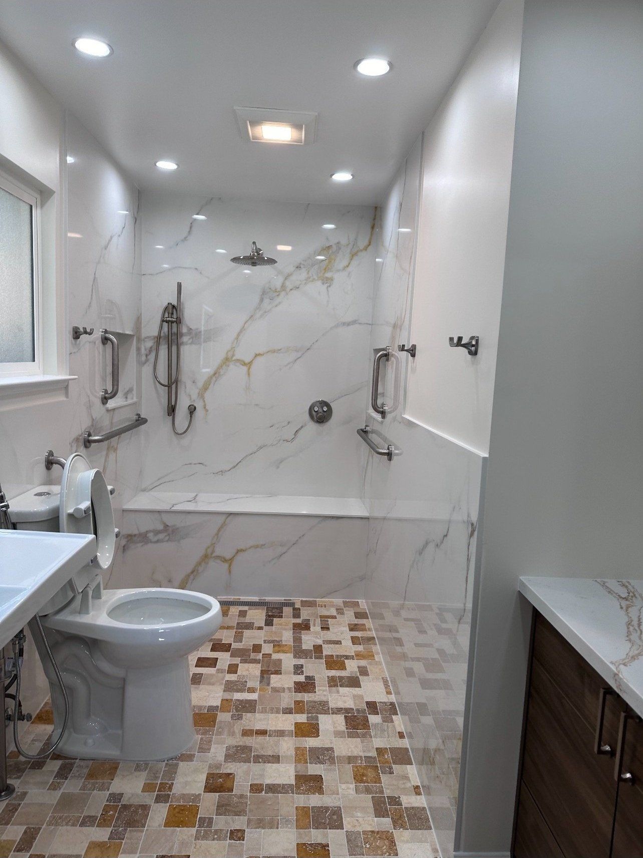 Accessible bathroom with marble-tiled shower and bench, grab bars, and mosaic tile floor.