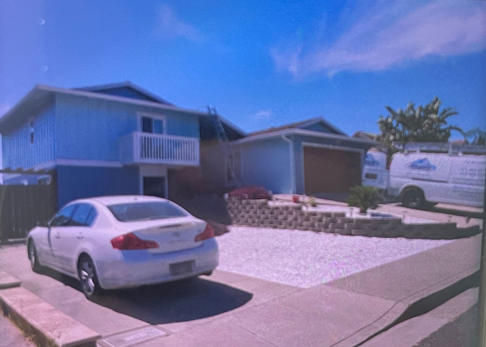 Blue house with white car parked in front, gravel yard, and garage.