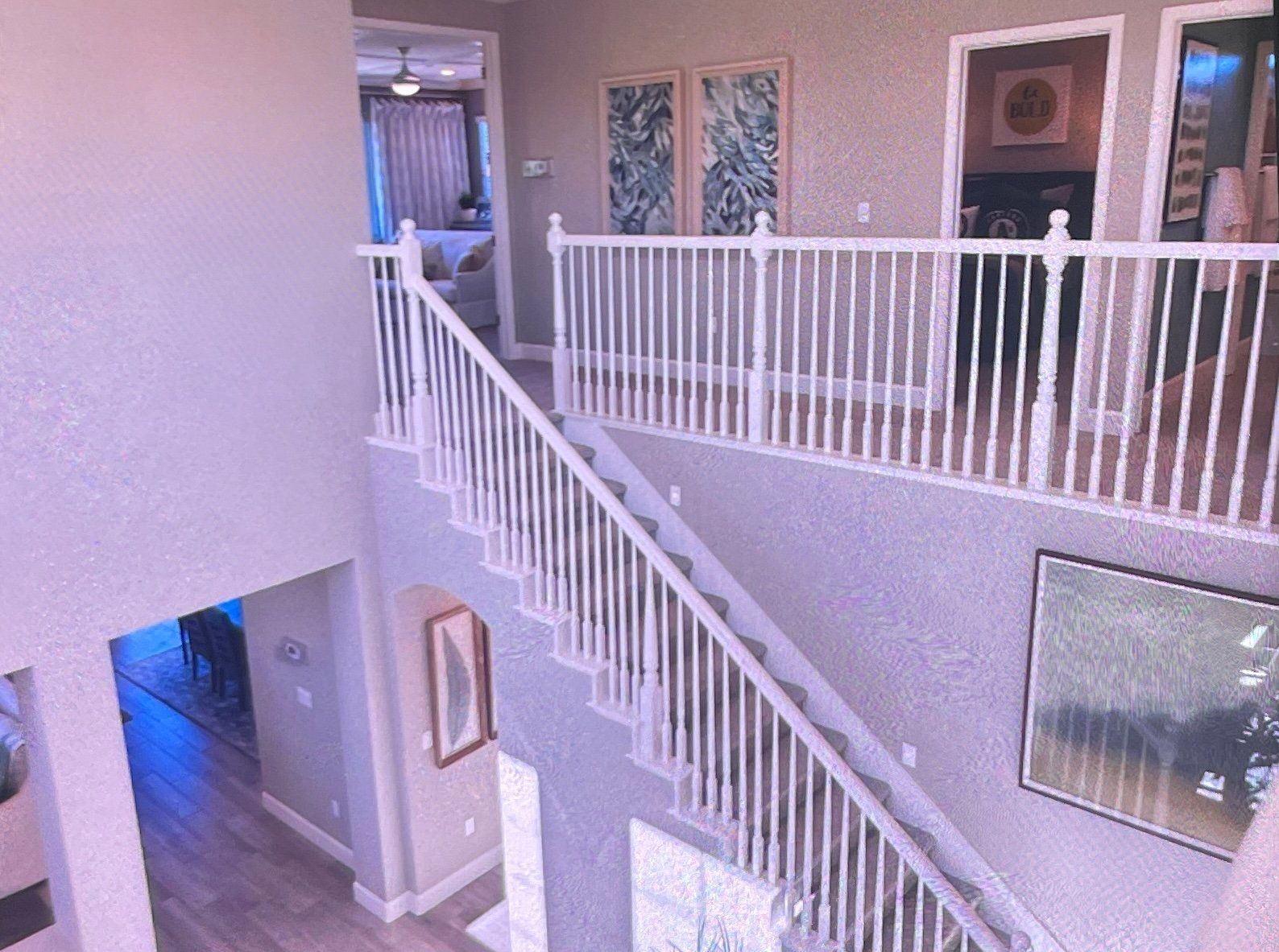 A two-story interior with a white staircase, landing, and railing. Artwork decorates the walls.