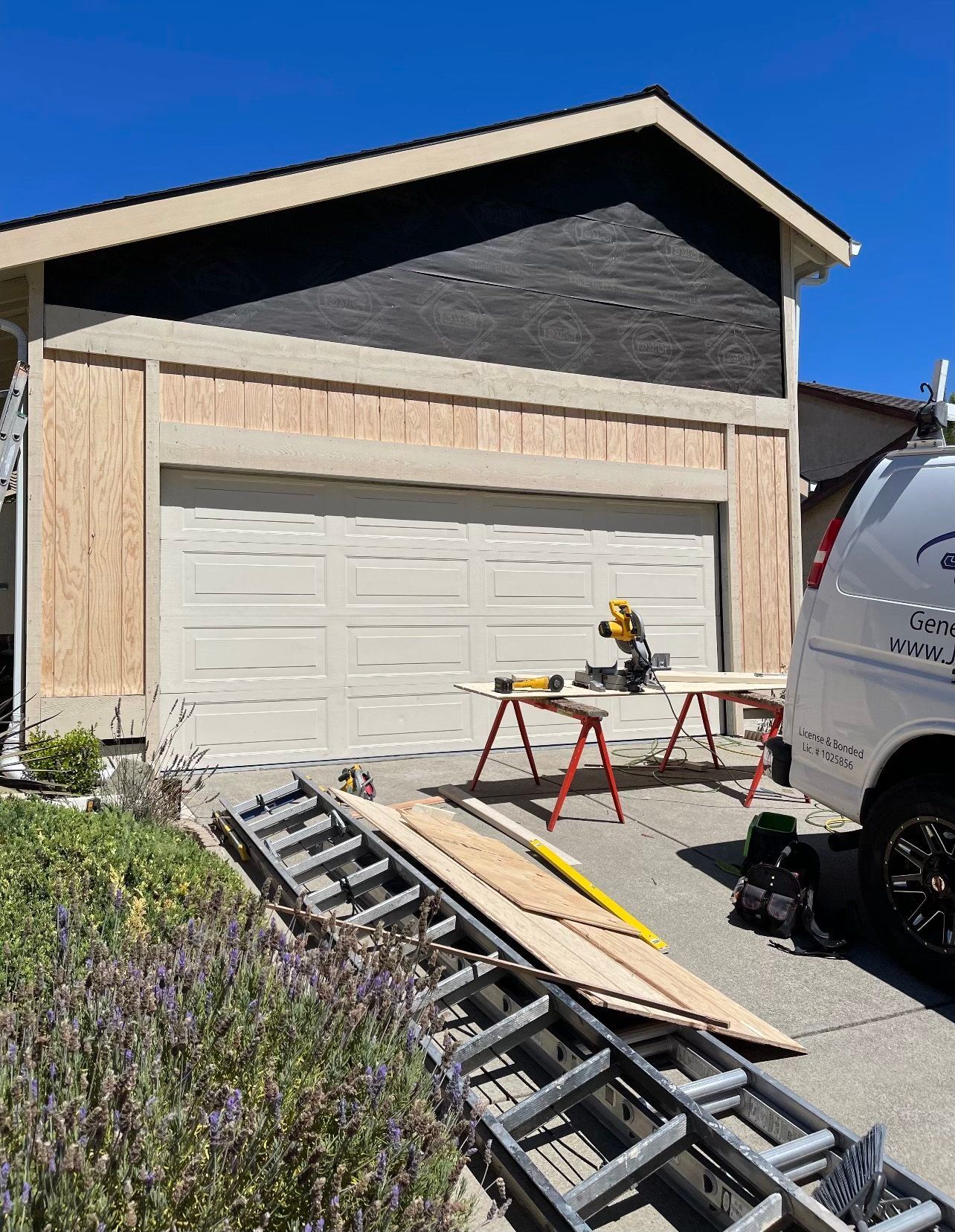 Garage exterior renovation in progress; siding partially installed, tools and materials present.