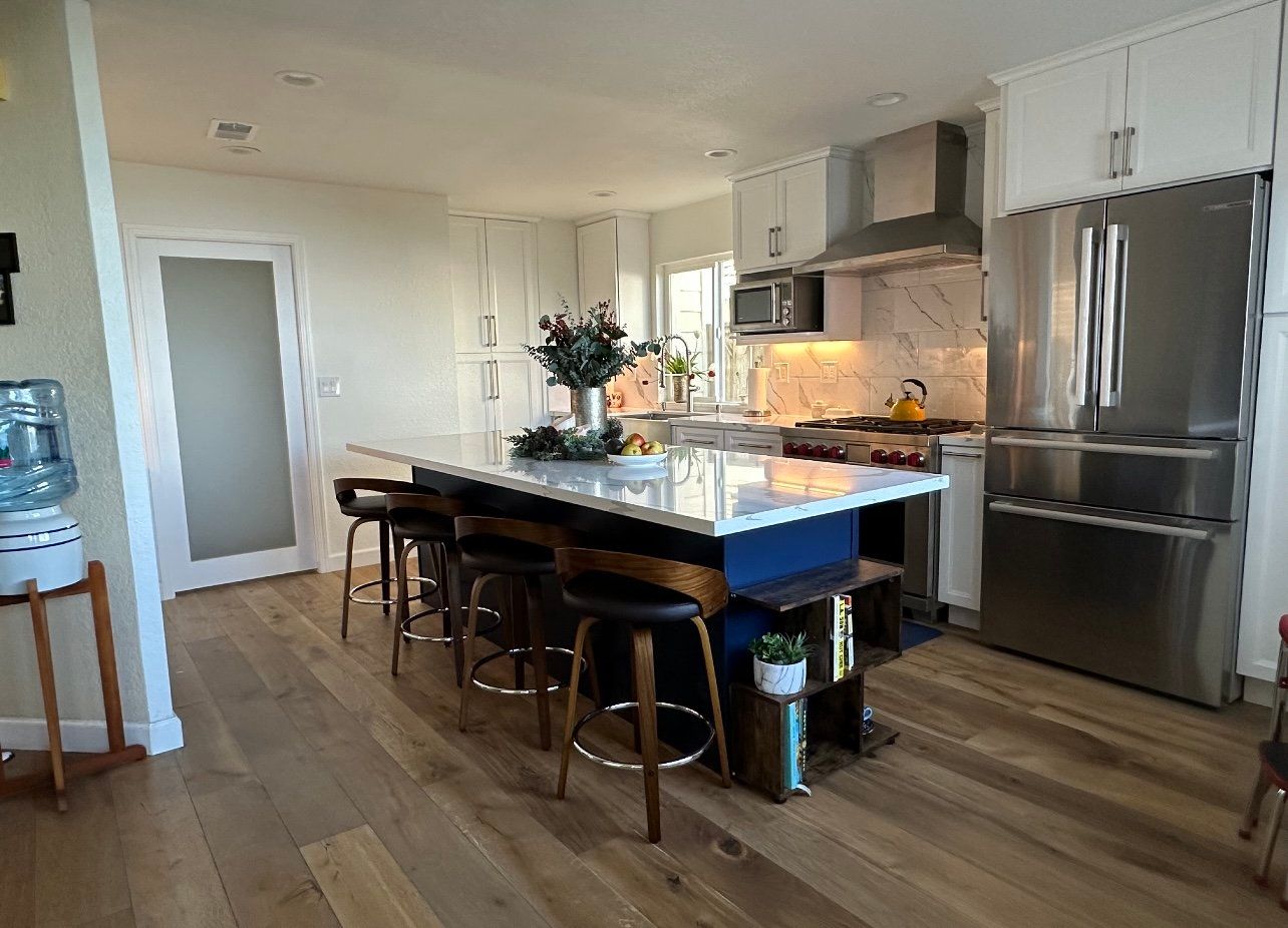 Kitchen with island, stainless steel appliances, white cabinets, and wood flooring.