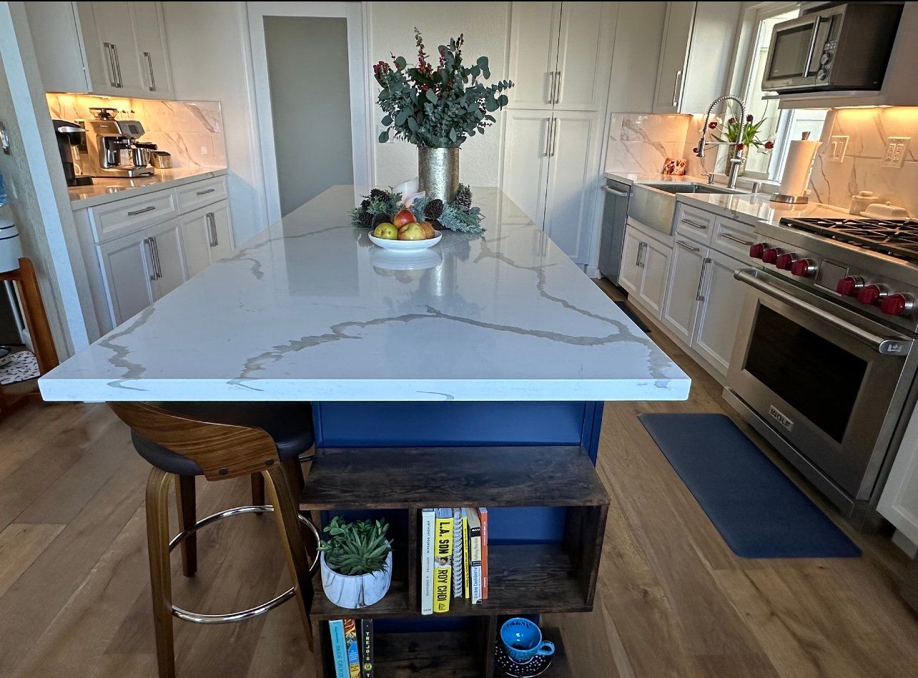 Kitchen with white cabinets, blue island, and quartz countertop. Includes a wooden stool and built-in bookshelf.