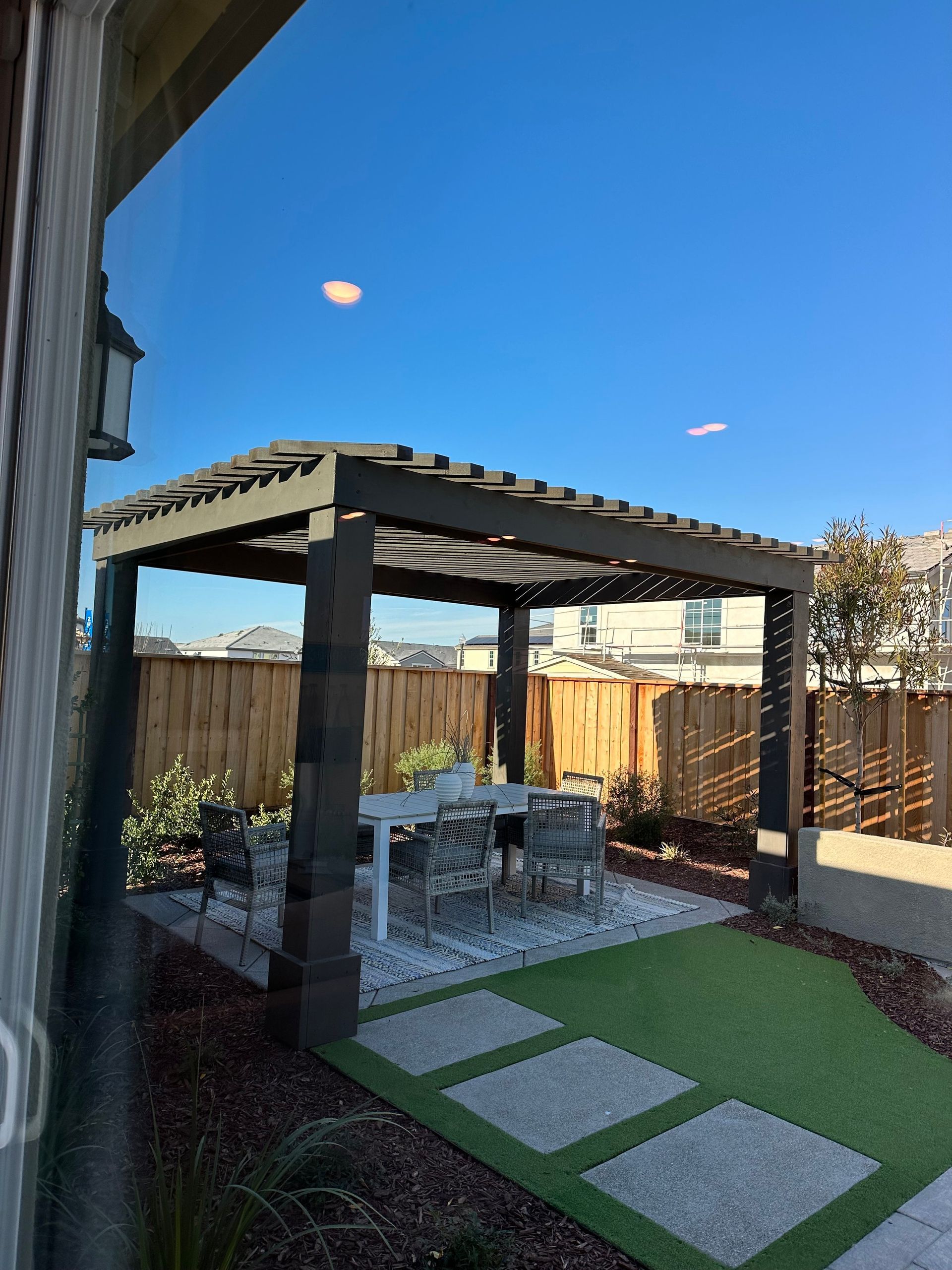 Pergola over outdoor dining set on patio with artificial grass and gravel.