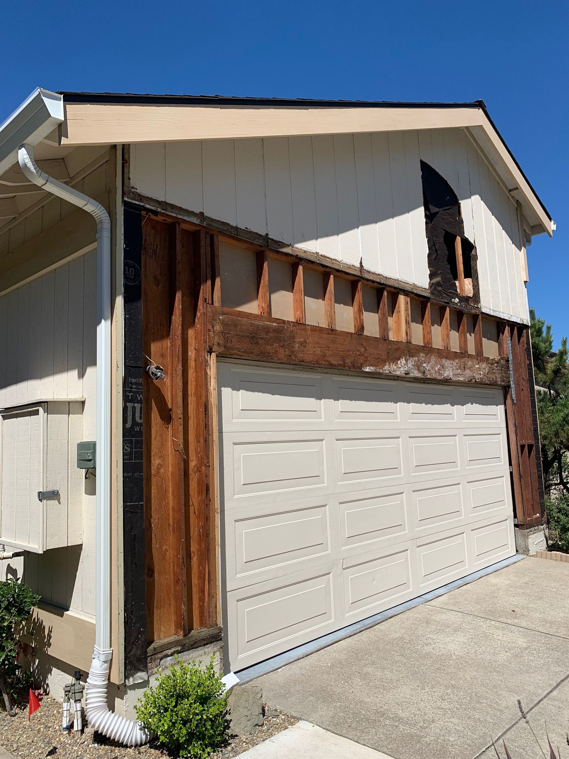 Garage with exposed wood framing, weathered siding, and a partially open garage door against a blue sky.