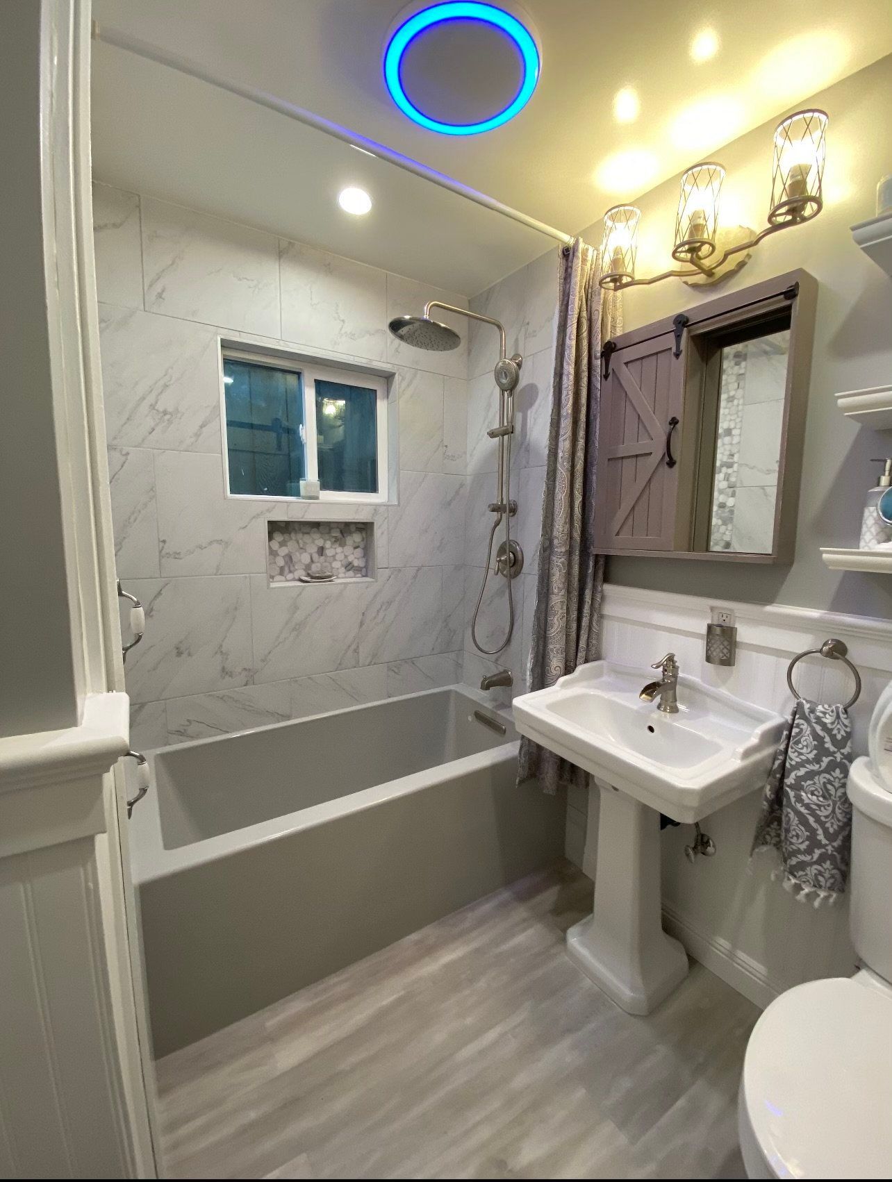 Bathroom with gray tub, white pedestal sink, and marble-like tile.