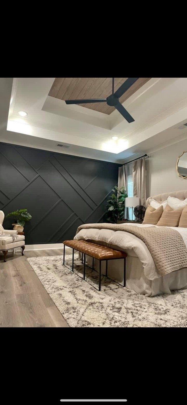 Bedroom with a dark accent wall, beige bedding, and a brown leather bench. Ceiling fan and rug.
