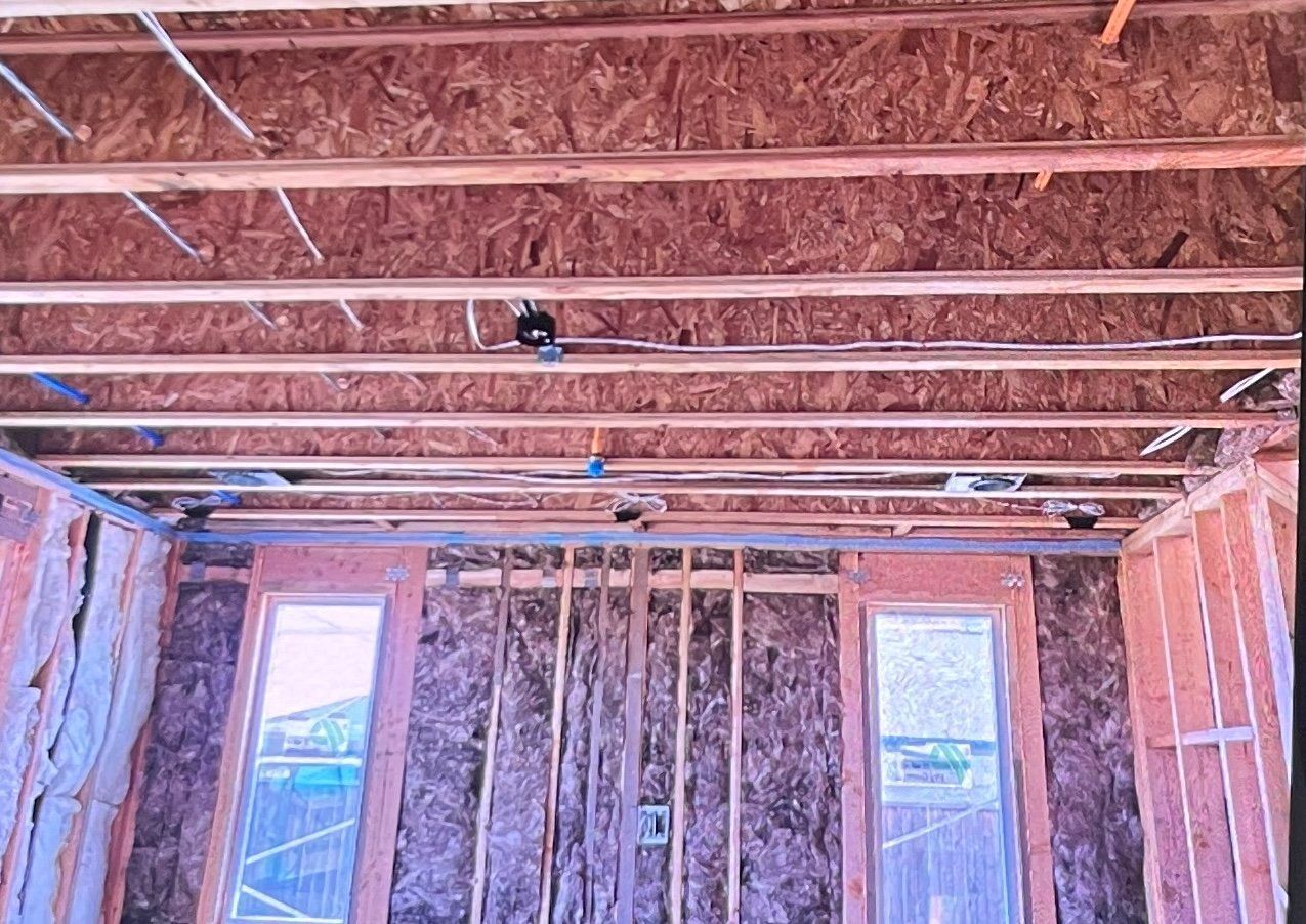 Interior view of a building under construction, showing exposed beams, insulation, windows, and electrical components.