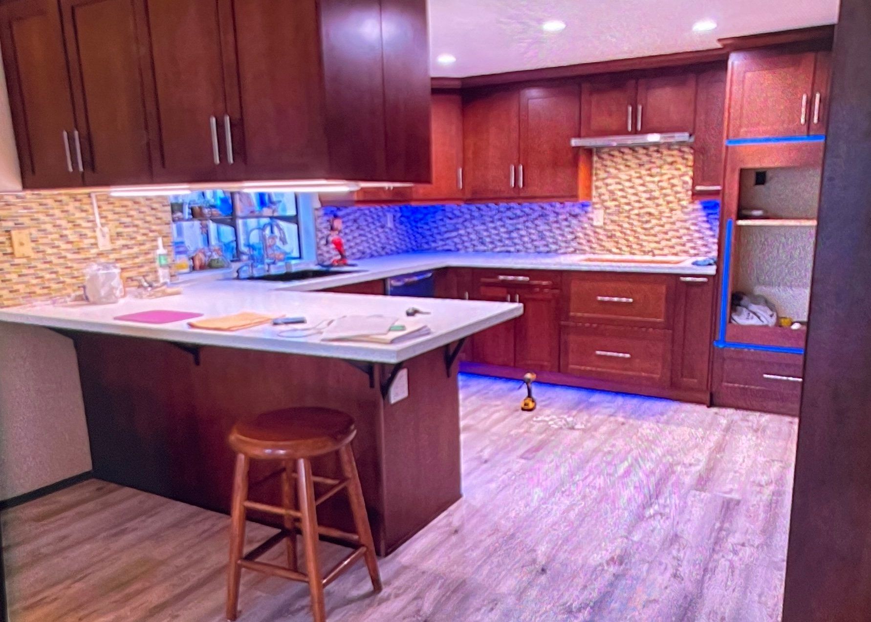 Kitchen with dark wood cabinets, white countertops, and tan tile backsplash, under cabinet lighting.
