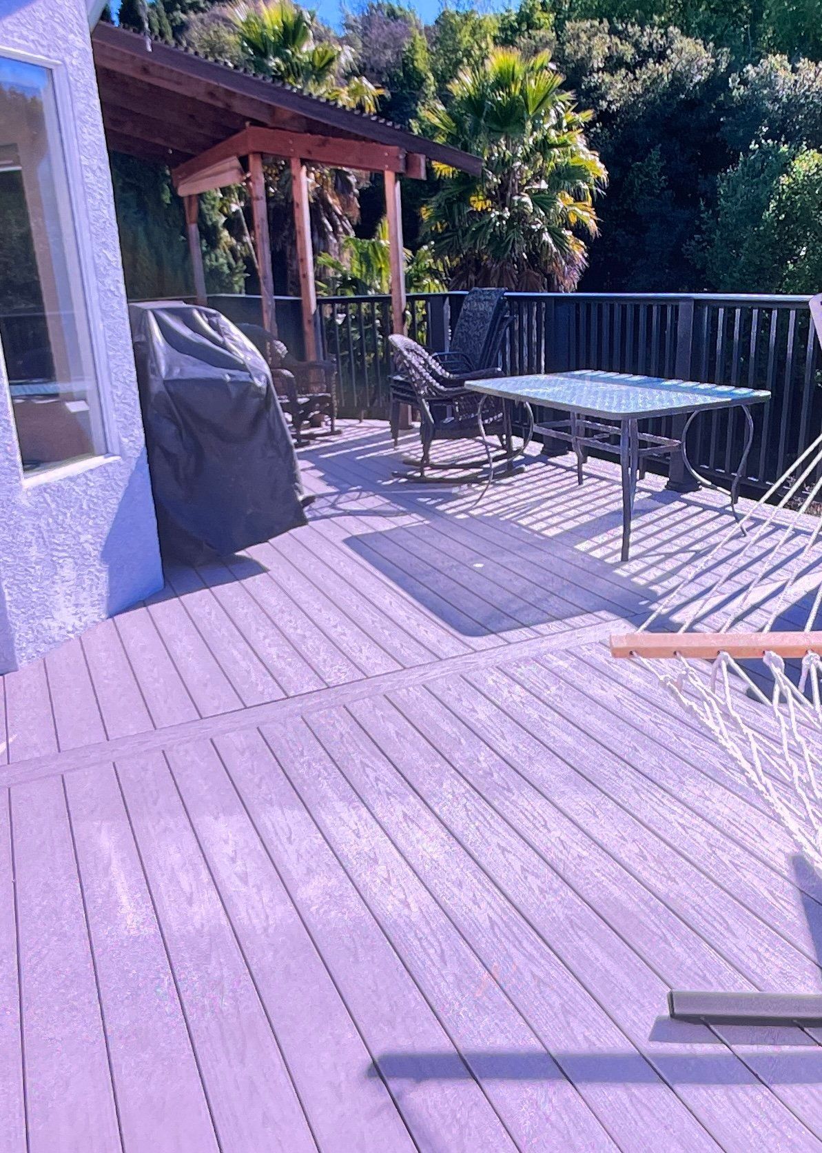 Wooden deck with table and chairs, covered grill, and gazebo with palm trees in the background.