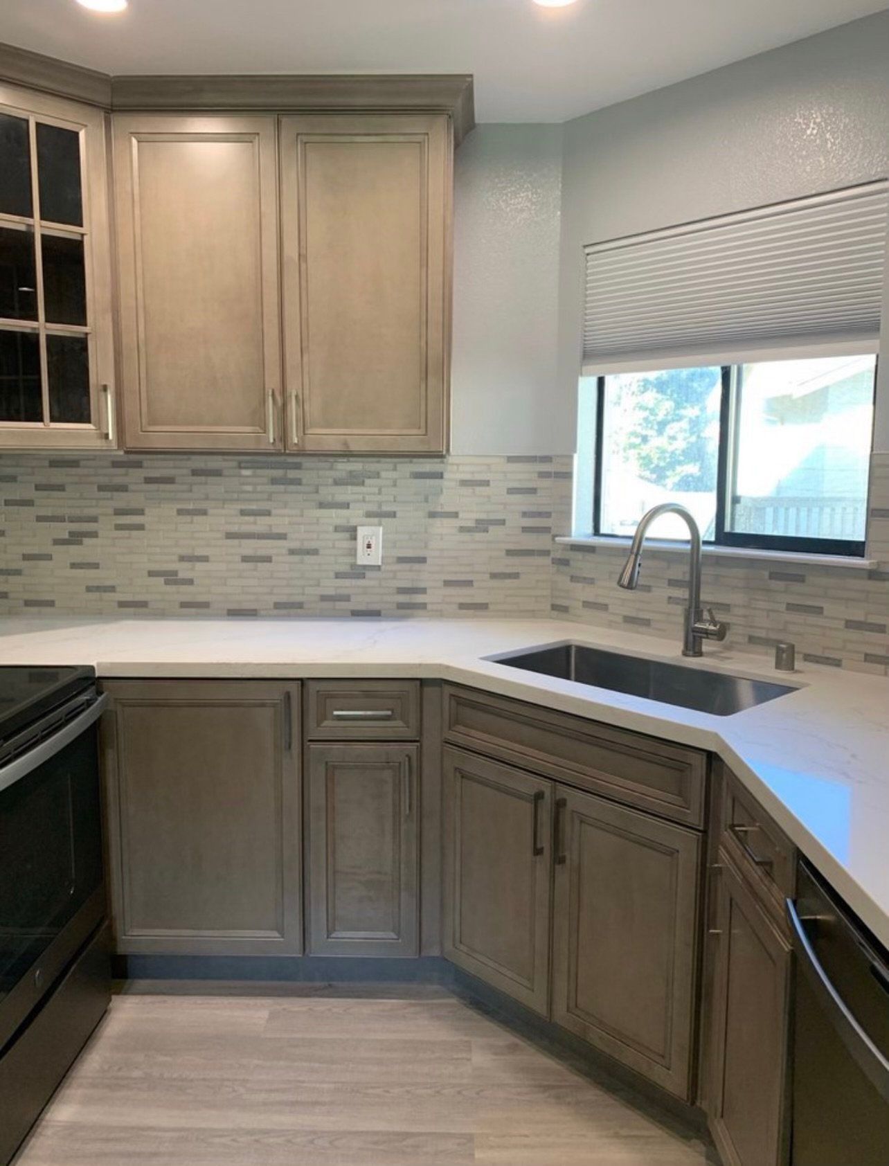 Kitchen with gray cabinets, white countertops, stainless steel sink, and gray backsplash.