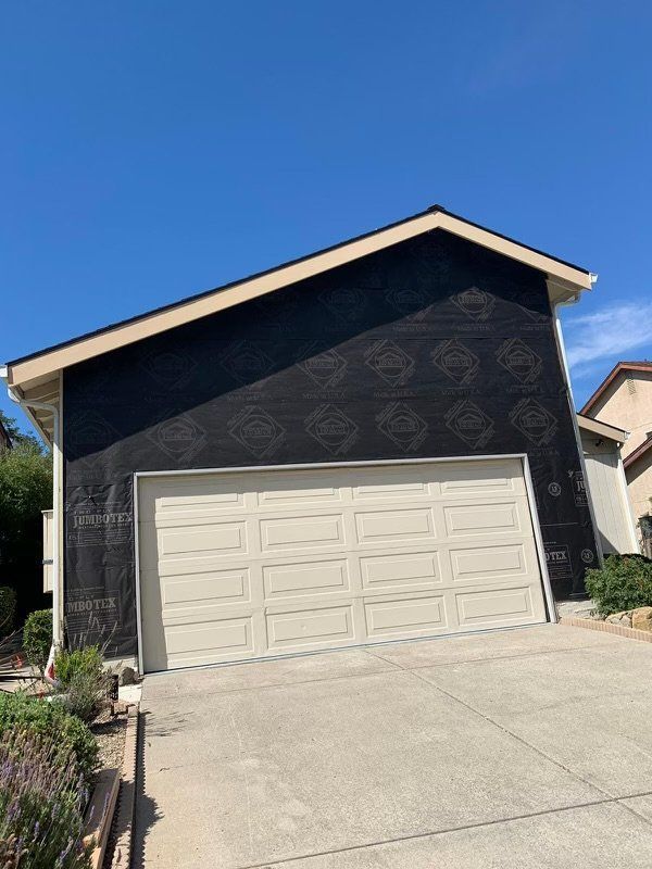 Garage with beige door, black sheathing on the upper portion, and a concrete driveway. Sunny, daytime.