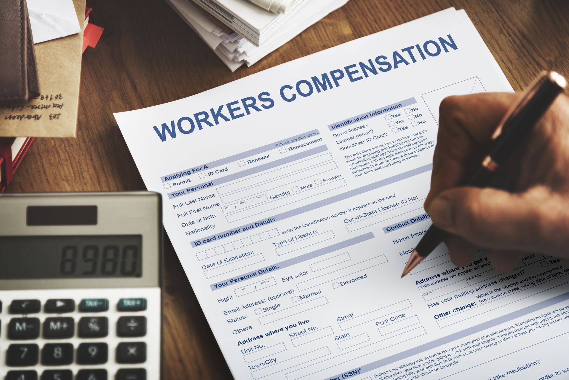 A person is filling out a workers compensation form next to a calculator