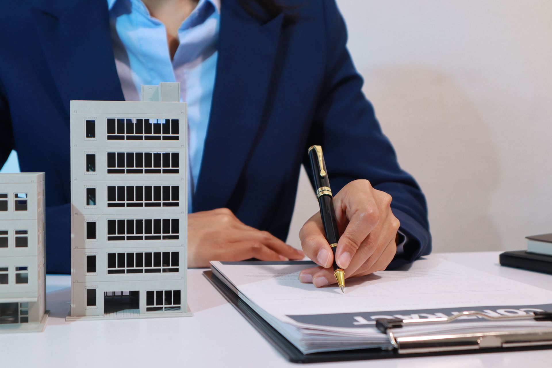 A woman is sitting at a desk writing on a clipboard next to a model of a building.