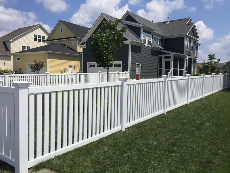 A white fence surrounds a large house in a residential area.