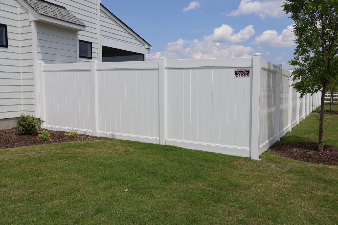 A white fence surrounds a lush green yard in front of a house.