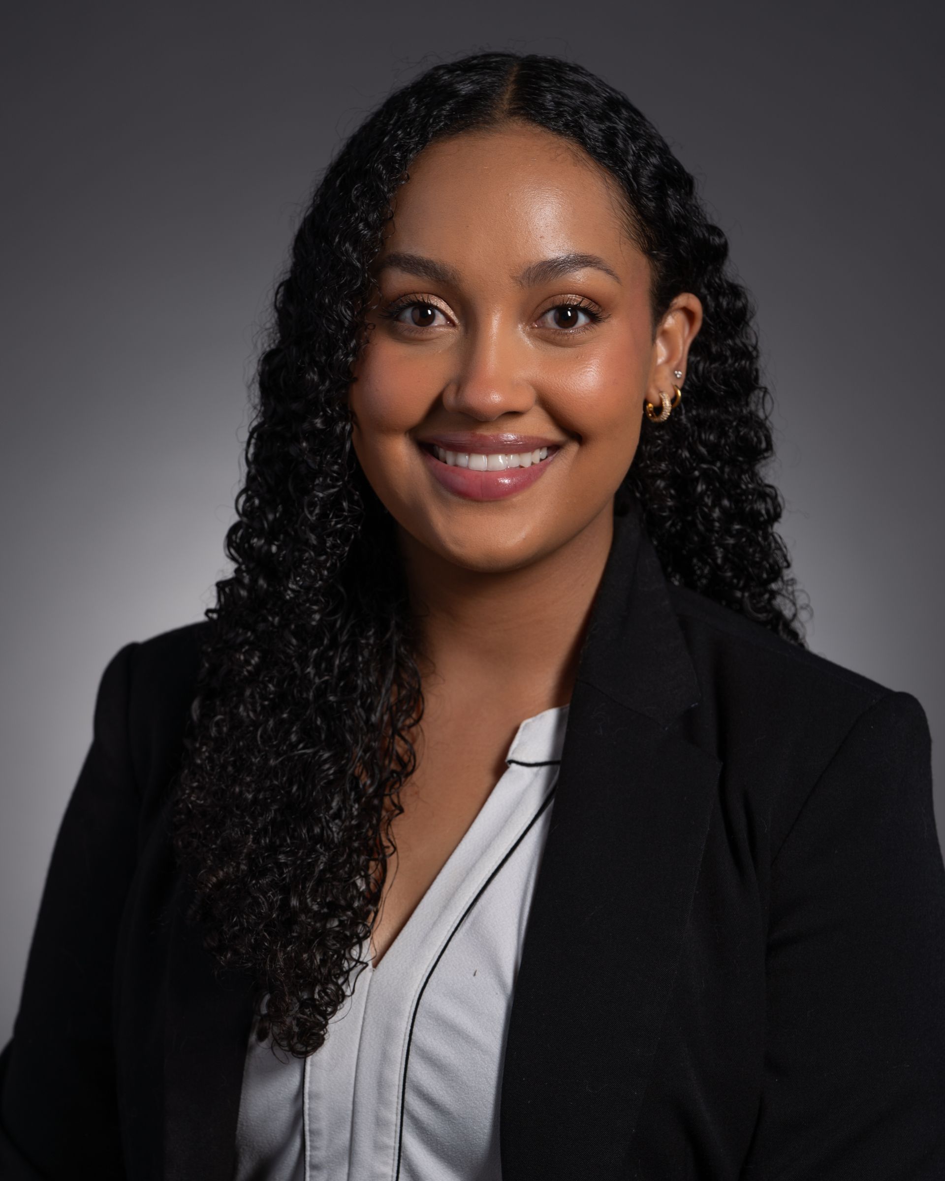 A woman with curly hair is wearing a black jacket and a white shirt.