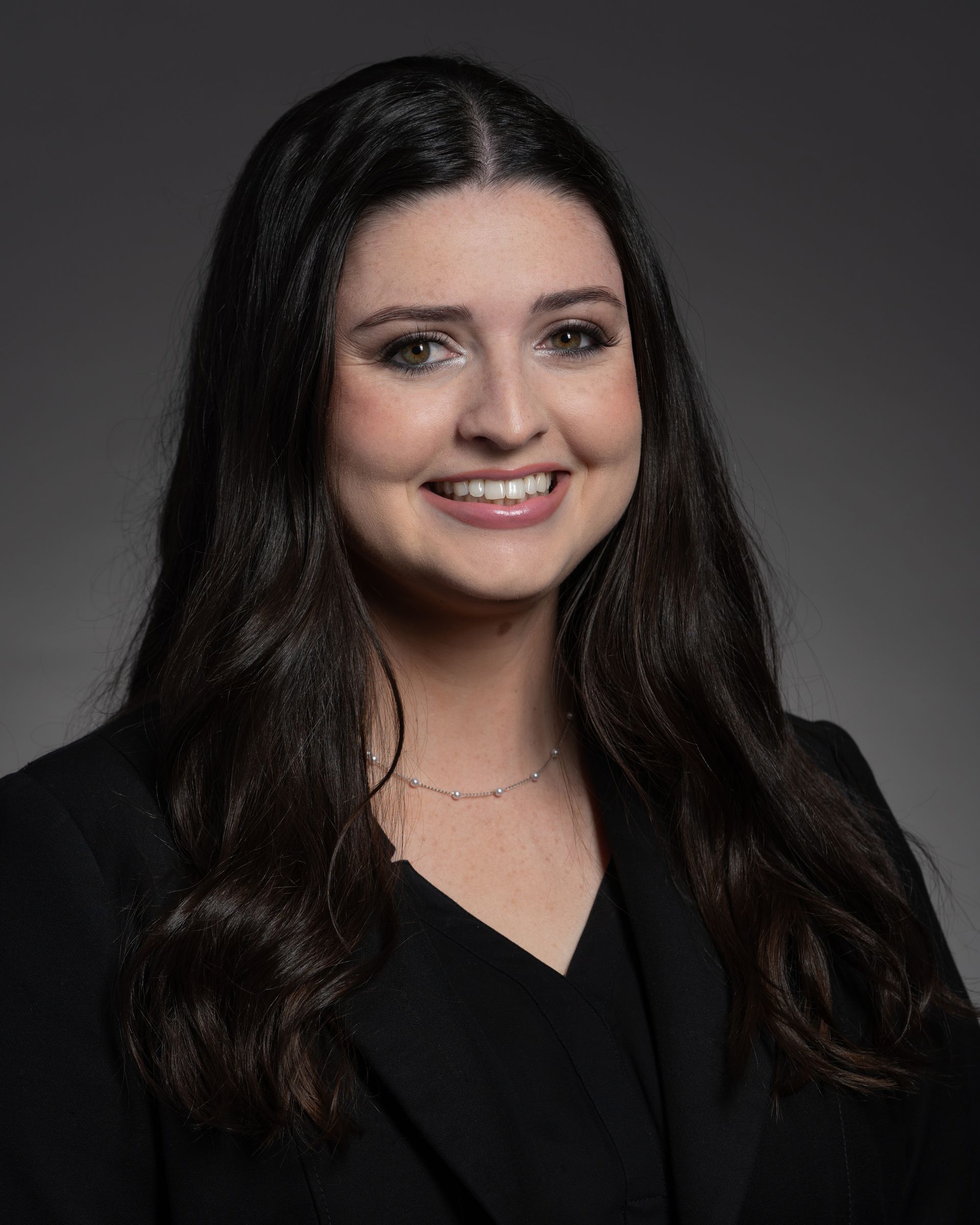 Woman with dark hair and a blazer smiles at the camera.