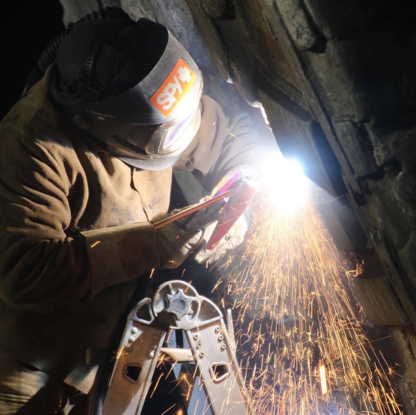 A man wearing a sky welding helmet is welding a piece of metal