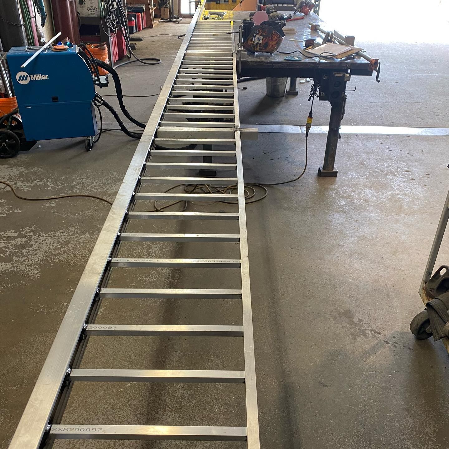 A long ladder is in a garage next to a miller welding machine