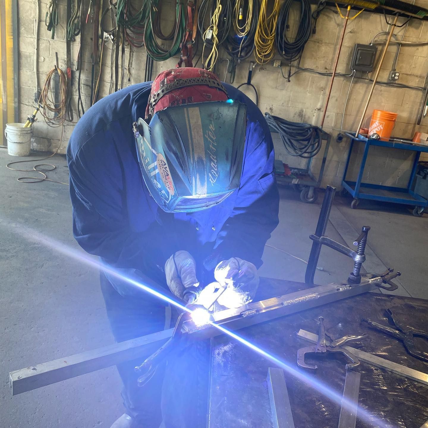A man wearing a welding mask is welding a piece of metal