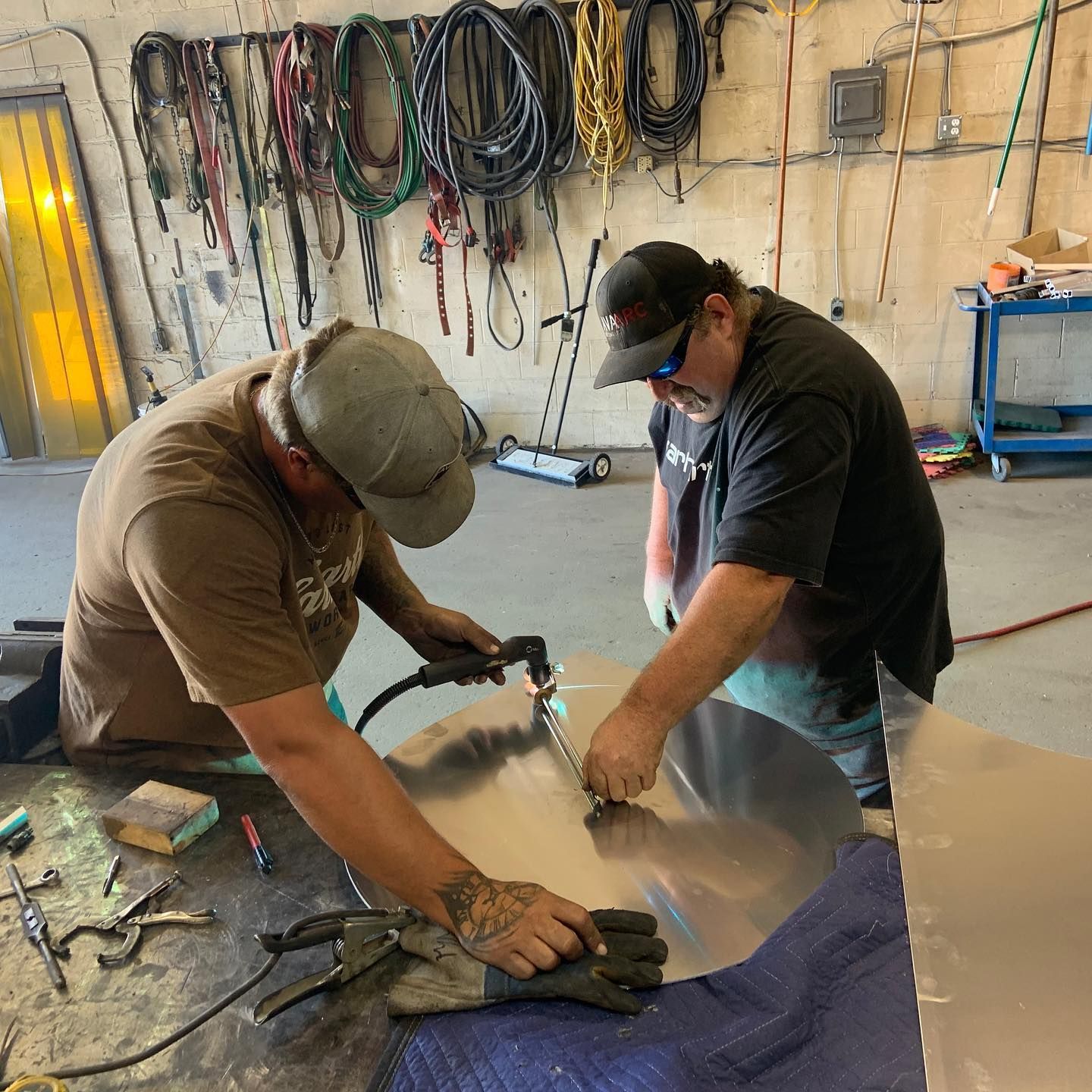 Two men are working on a piece of metal in a garage