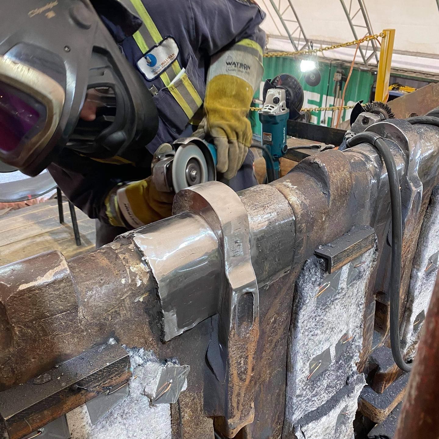 A man wearing a welding helmet is grinding a piece of metal
